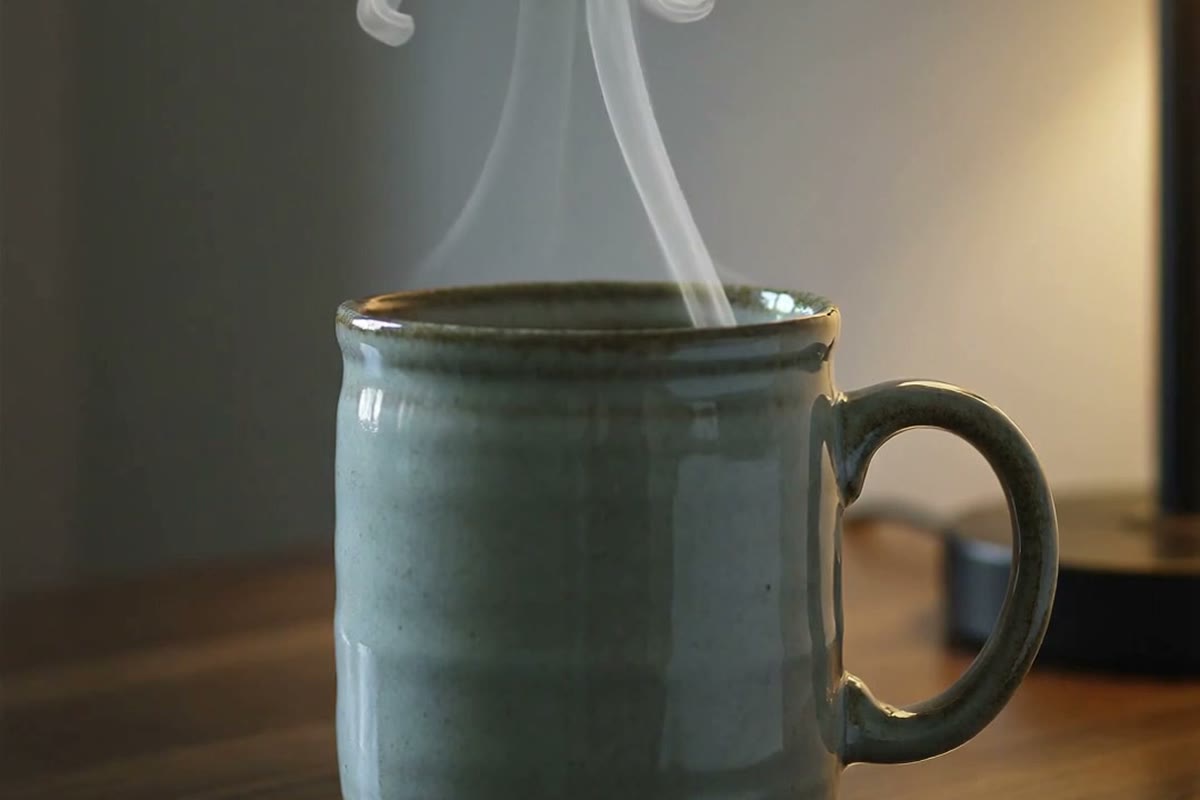 A steaming mug of herbal tea beside a warm lamp in the evening