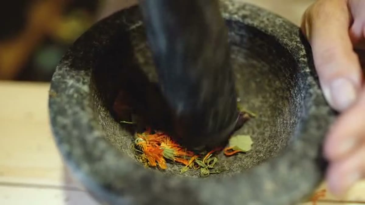 A pestle grinding dried flowers and herbs in a granite mortar