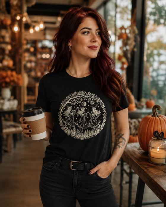 Witch Dance Tee — three witches dancing under a botanical moon, cream print on a black tee